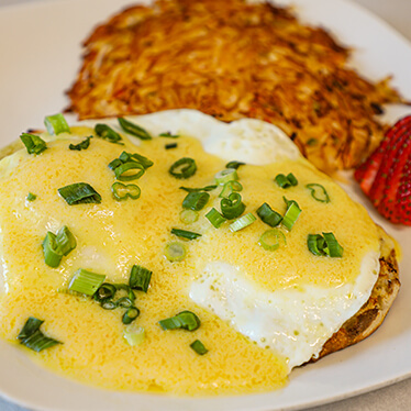 Fried eggs on a toasted English muffin topped with Hollandaise sauce and a side of hash browns.