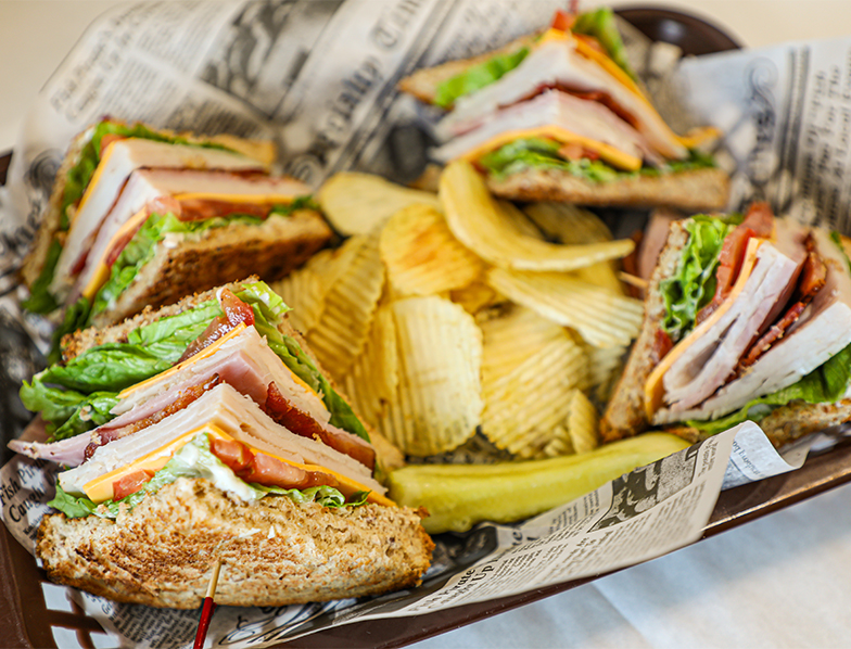 A delicious turkey club served with a side of crispy potato chips and a tangy pickle in a woven basket.