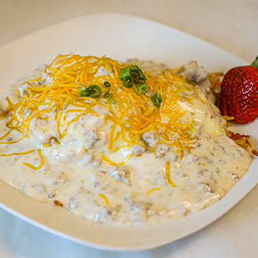 A plate of biscuits and gravy topped with shredded cheddar cheese and chopped green onions.